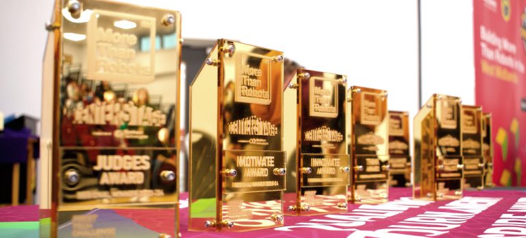 A row of gold trophies sitting on a table covered in fabric with a pull up banner in the background